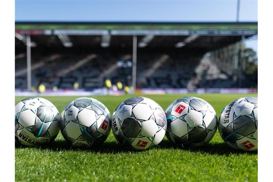 Fußbälle liegen vor der Tribüne auf dem Rasen. Foto: Patrick Seeger/dpa