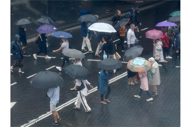 Fußgänger schützen sich mit Regenschirmen vor starkem Regen. Der Niederschlag bringt angesichts der anhaltenden Buschbrände in New South Wales etwas Entlastung für die Einsatzkräfte. Foto: Bianca De Marchi/AAP/dpa