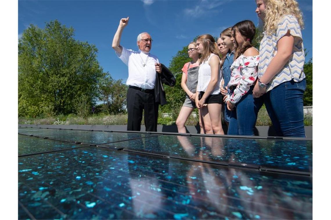 Gebhard Fürst, Bischof der Diözese Rottenburg-Stuttgart, steht mit Schülern hinter Solarmodulen. Foto: Marijan Murat