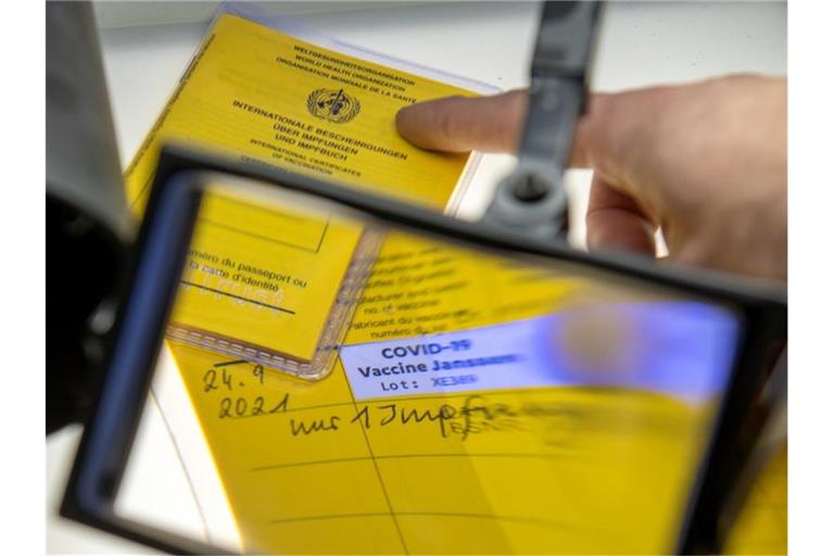 Gefälschte Impfpässe unter einer Lupe (Symbolbild). Foto: Stefan Puchner/dpa