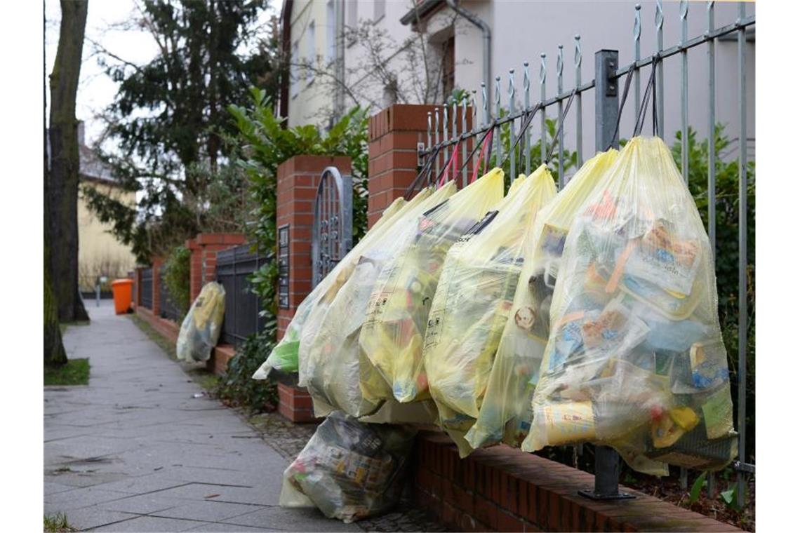 Gefüllte gelbe Müllsäcke hängen in einer Straße am Gartenzaun. Foto: Jens Kalaene/dpa-Zentralbild/dpa/Symbolbild