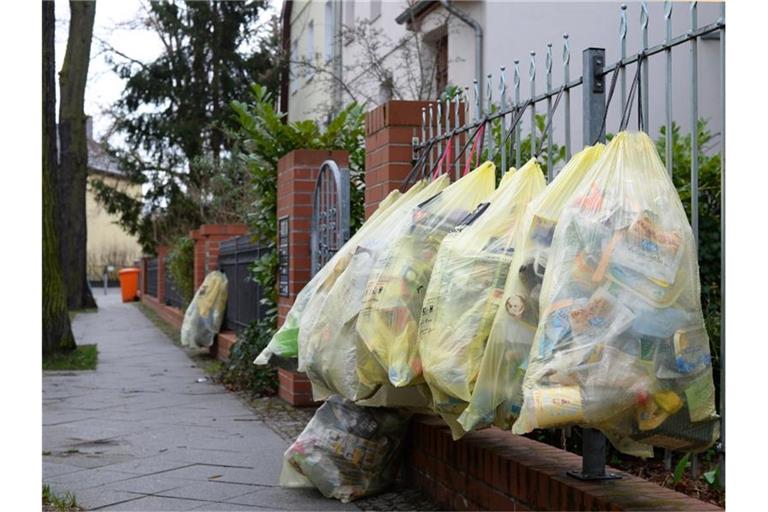 Gefüllte gelbe Müllsäcke hängen in einer Straße am Gartenzaun zur Abholung bereit. Foto: Jens Kalaene/dpa-Zentralbild/dpa