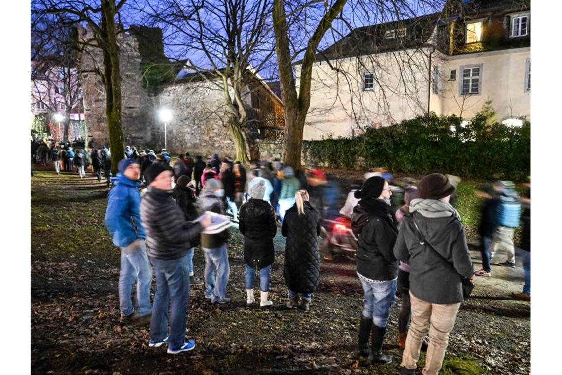 Knapp 56.000 Teilnehmer bei Corona-Demos am Montagabend Gegner der Coronapolitik gehen durch die Innenstadt von Ravensburg, während mehrere Passanten sich den Demonstrationszug anschauen und einer nebenbei Pizza isst. Foto: Felix Kästle/dpa