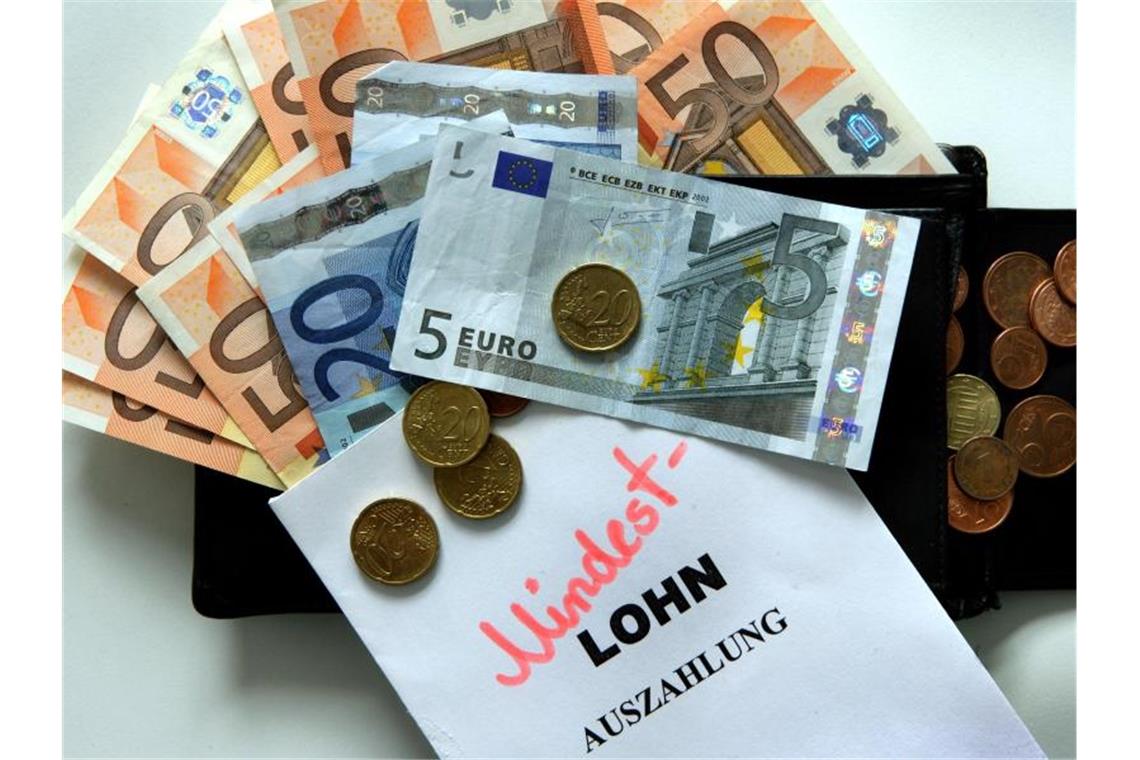 Viele Menschen arbeiten für unter zwölf Euro die Stunde Geld liegt neben einem Zettel mit der Aufschrift „Mindestlohn“. Foto: Jens Büttner/dpa-Zentralbild/dpa/Symbolbild