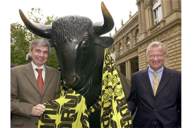 Gerd Niebaum (r), damaliger BVB-Präsident, und der damalige BVB-Manager Michael Meier stehen am 31.10.2000 vor der Frankfurter Börse mit einem übergroßen Fanschal am Bronzebullen. Foto: Arne Dedert/dpa/Archivbild
