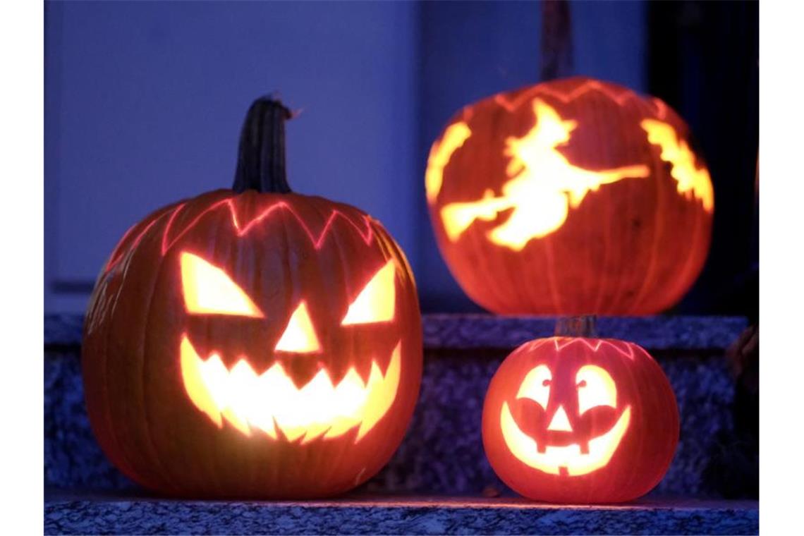 Geschnitzte Halloween-Kürbisse mit Geister-Motiven stehen von innen beleuchtet vor einem Haus. Foto: Bernd Weissbrod/dpa/Archivbild