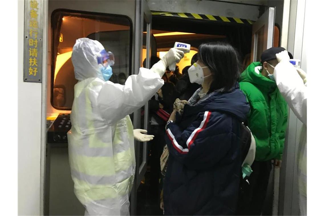 Gesundheitsbeamte kontrollieren in Peking die Körpertemperatur aus Wuhan angereister Passagiere. Foto: Emily Wang/AP/dpa