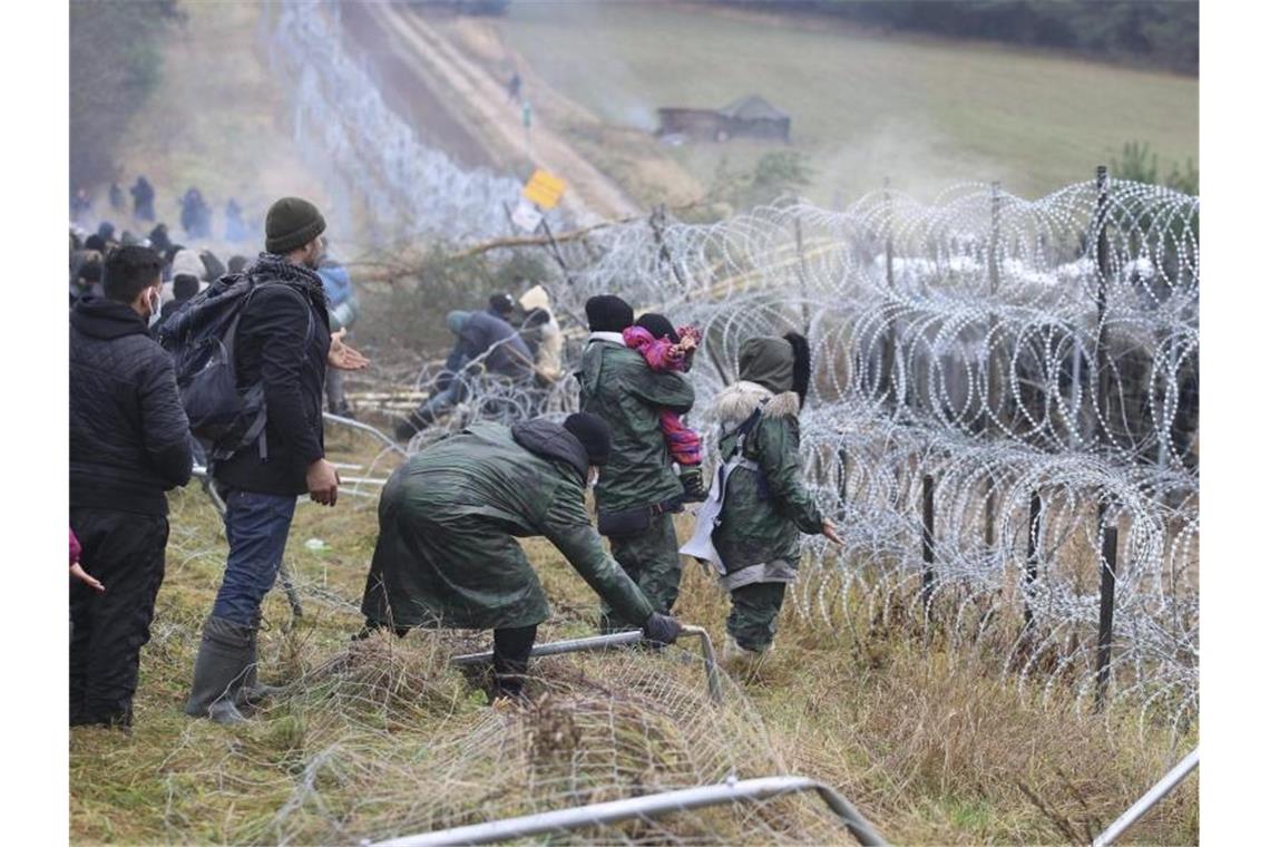 EU-Kommission will Asylregeln an Belarus-Grenze aussetzen Getrennt durch Stacheldraht: Migranten stehen an der Grenze auf der belarussischen Seite - auf der polnischen stehen Sicherheitskräfte. Foto: Leonid Shcheglov/BelTA/AP/dpa