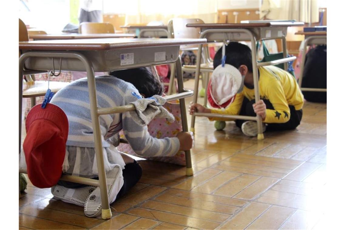 Grundschüler suchen während einer Erdbeben-Notfallübung in Usuki Schutz unter ihren Tischen. Foto: -/kyodo/dpa
