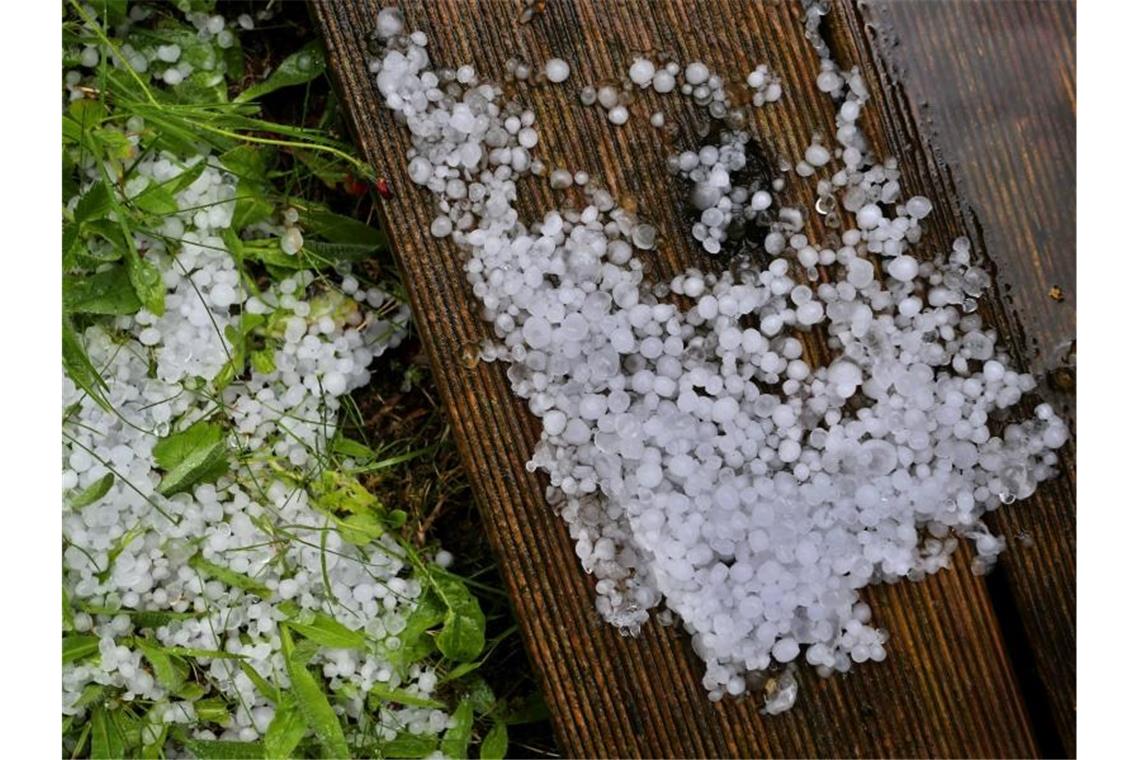 Hagelkörner liegen in einem Garten auf einer Holzterrasse und dem Rasen. Foto: Karl-Josef Hildenbrand/dpa/Symbolbild