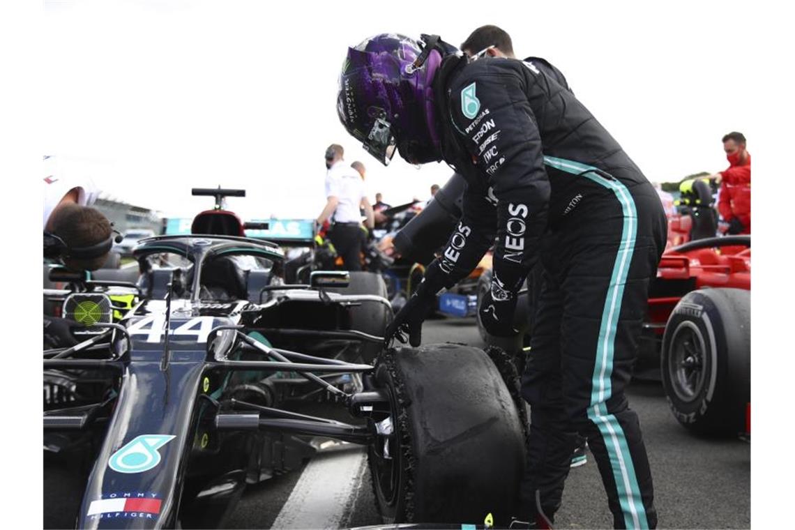 Hamilton schaut sich im Zielbereich den kaputten Reifen an. Foto: Bryn Lennon/Pool Getty/AP/dpa