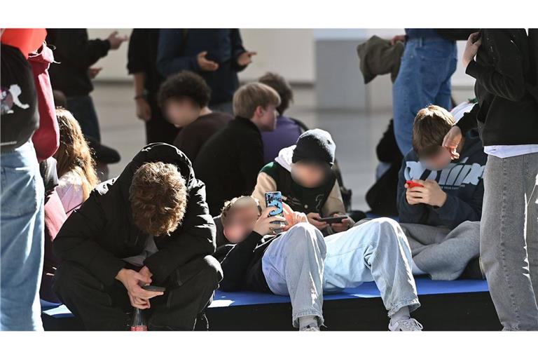 Handy-Sucht: Schüler sitzen während der Pause auf dem Boden und blicken auf ihre Smartphones.