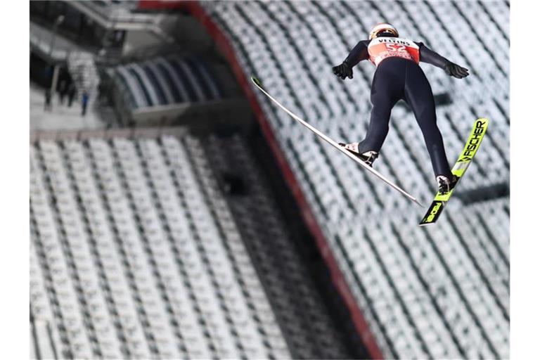 Hat das erste Springen der Vierschanzentournee gewonnen: Karl Geiger schwebt vor der leeren Tribüne in Oberstdorf. Foto: Daniel Karmann/dpa