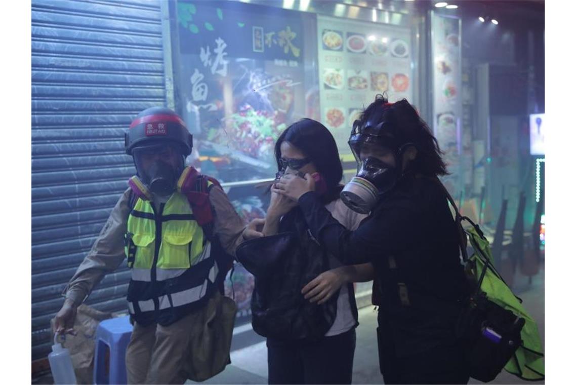 Helfer tragen Atemschutzmasken und begleiten eine Protestteilnehmerin aus einer Tränengaswolke. Foto: Kin Cheung/AP/dpa