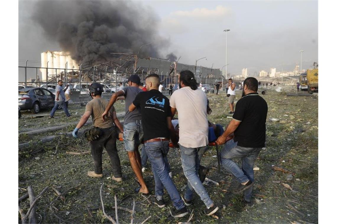Helfer tragen ein Opfer weg, während im Hintergrund Rauch aufsteigt. Foto: Hussein Malla/AP/dpa