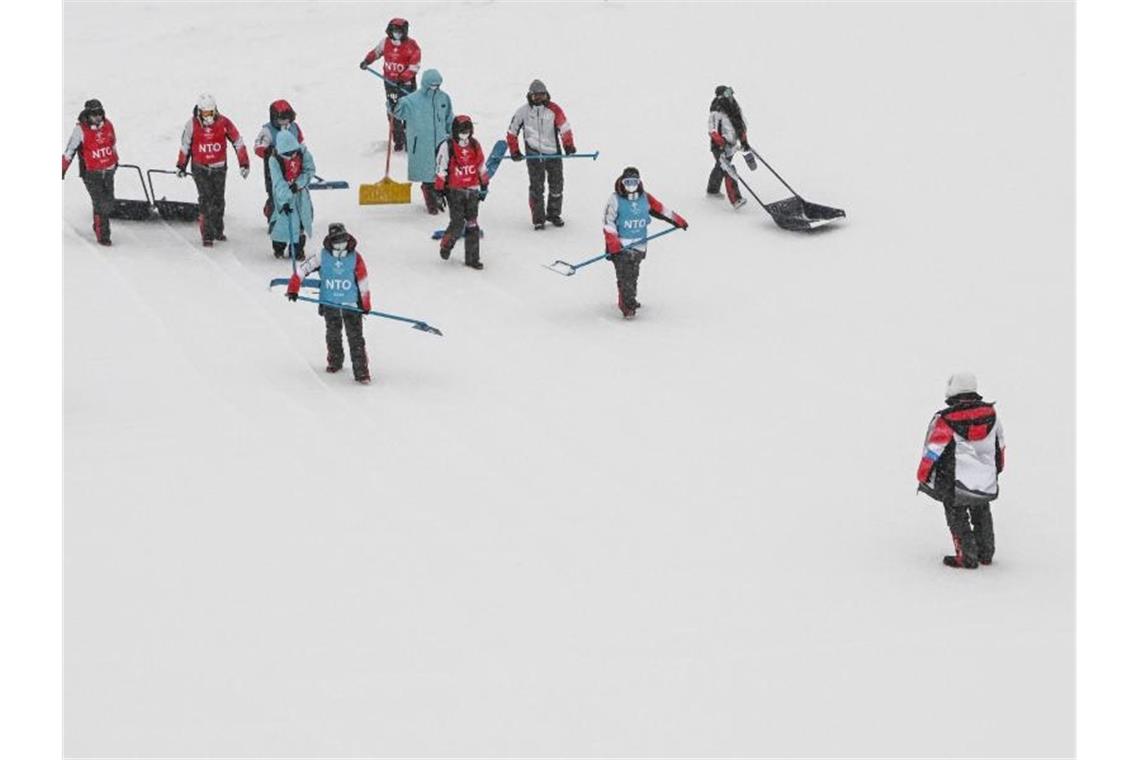 Helfer versuchen die Slopestyle-Piste vom Schnee zu befreien. Foto: Angelika Warmuth/dpa
