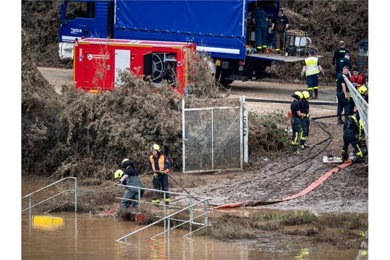Helfer von Feuerwehr und Technischem Hilfswerk (THW) pumpen Wasser aus einem Regenrückhaltebecken ab, in dem sich noch Fahrzeuge befinden sollen. Foto: Marius Becker/dpa