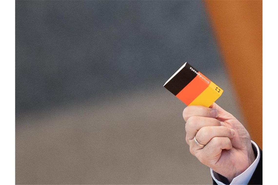 Herbert Reul (CDU), Innenminister von Nordrhein-Westfalen, hält bei seiner Rede im Plenum des Landtags ein kleines Buch mit dem Grundgesetz hoch. Foto: Rolf Vennenbernd/dpa