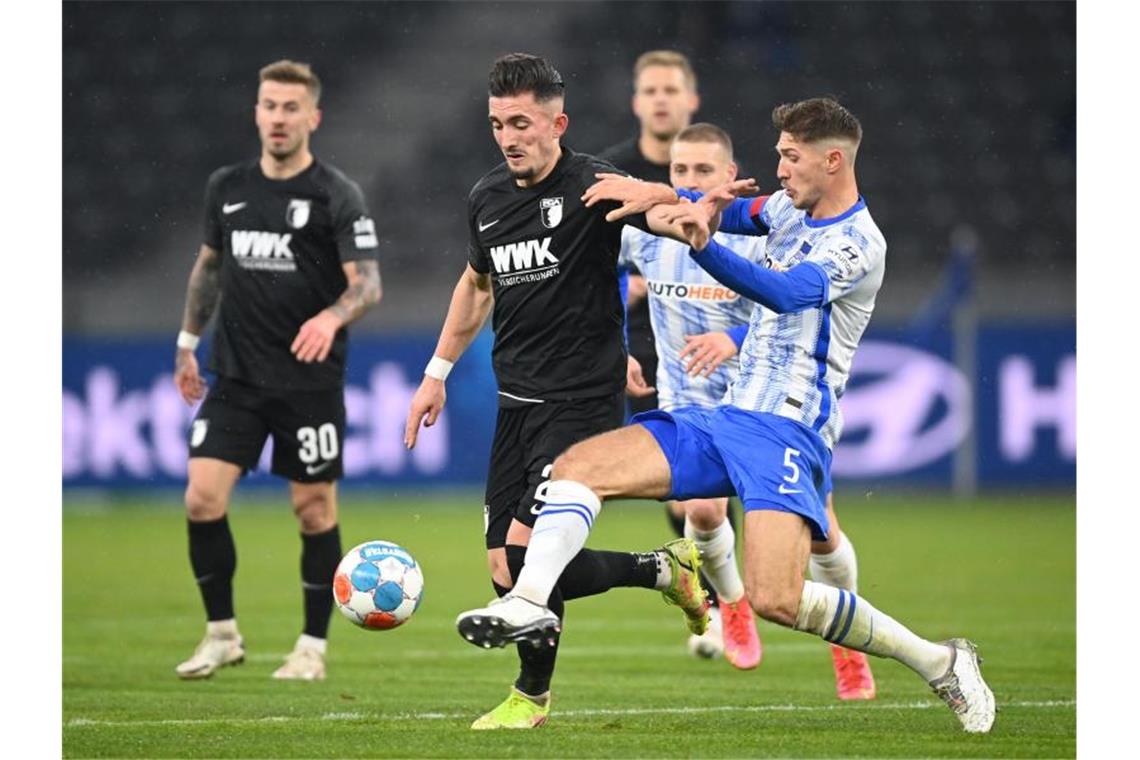 Herthas Niklas Stark (r) und Augsburgs Andi Zeqiri (M) kämpfen um den Ball. Foto: Soeren Stache/dpa-Zentralbild/dpa