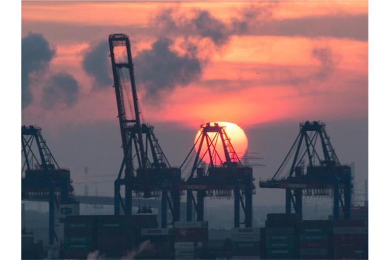 Hinter den Containerbrücken eines Terminals im Hamburger Hafen geht die Sonne unter. Foto: Christian Charisius/dpa