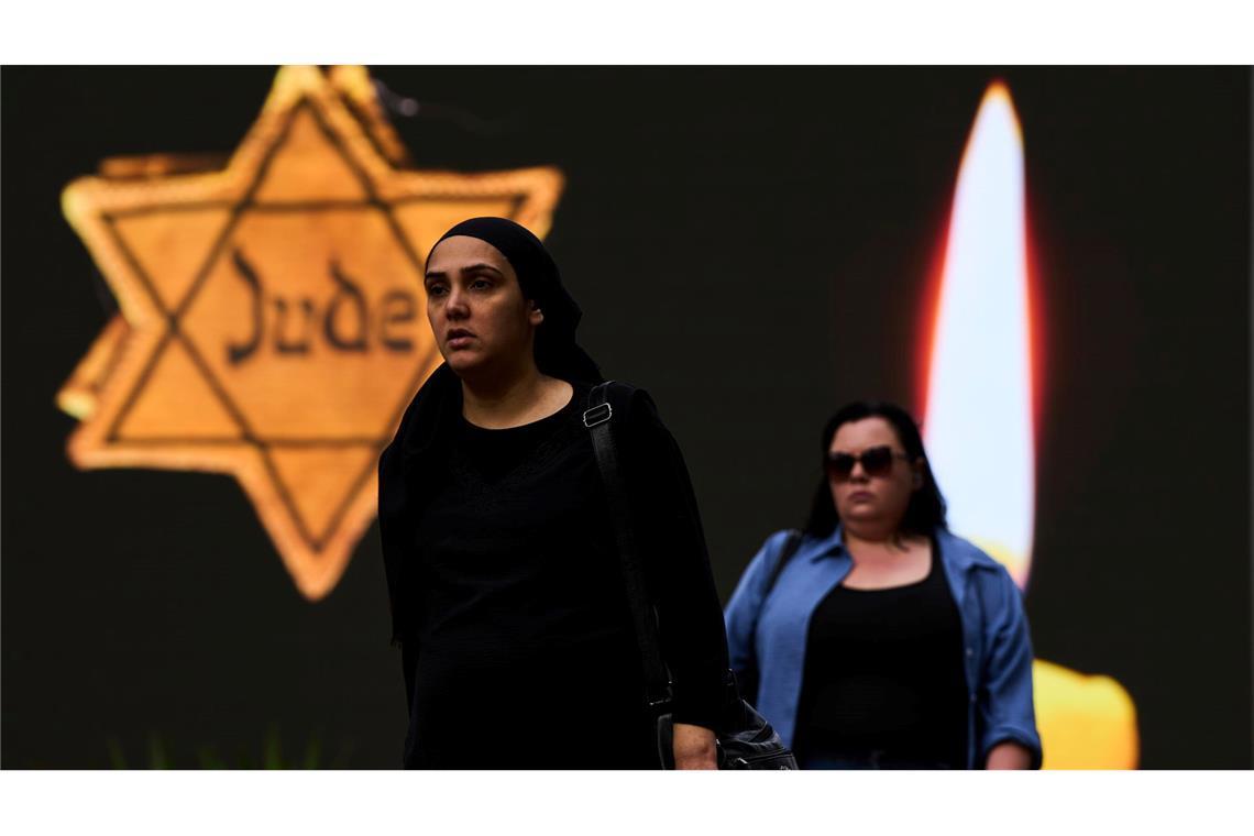 Bilder des Tages Holocaust-Gedenktag in Israel: Zwei Frauen gehen neben einer Plakatwand mit der Abbildung eines gelben Davidsterns, auf dem das Wort "Jude" steht, entlang.
