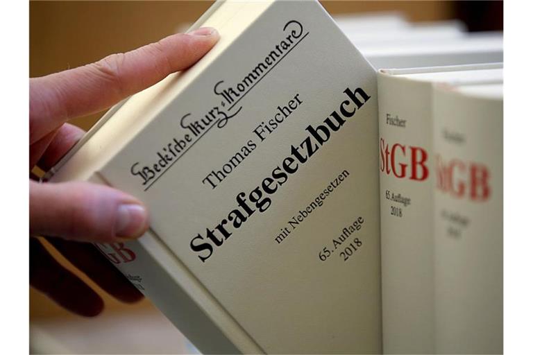 Illustration - Ein Jurist nimmt das Strafgesetzbuch aus dem Regal. In Bayern muss sich ein junger Polizist unter anderem wegen des Besitzes kinderpornografischer Schriften vor einem Gericht verantworten. Foto: Oliver Berg/dpa