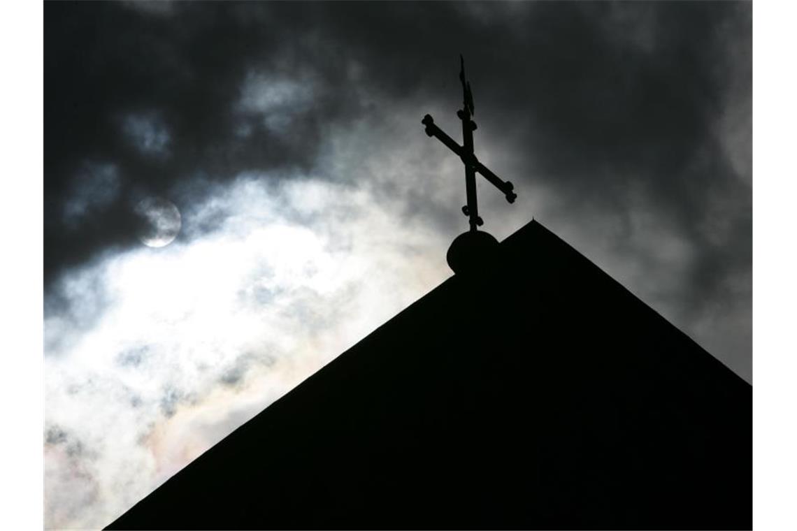 Im Gegenlicht und vor wolkenverhangenem Himmel ist die Kirchturmspitze eines Doms mit Kreuz zu sehen. Foto: Friso Gentsch/dpa/archiv