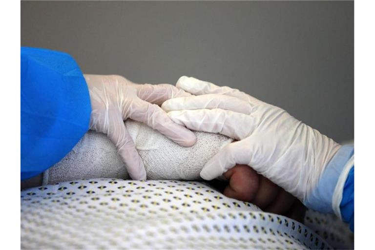 Im Infektionszimmer für Covid-19-Patienten auf der Interdisziplinären internistischen Intensivtherapiestation (ITS) der Universitätsmedizin Rostock halten Pflegekräfte die Hand eines Patienten im künstlichen Koma. Foto: Bernd Wüstneck/dpa-Zentralbild/dpa