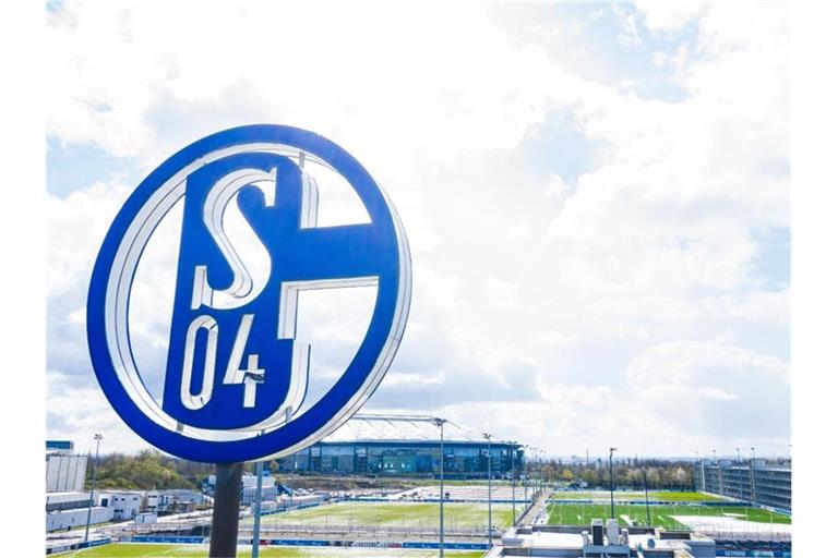 Im Vordergrund dreht sich das Logo des FC Schalke auf der Geschäftsstelle, im Hintergrund steht die Veltins-Arena. Foto: Guido Kirchner/dpa