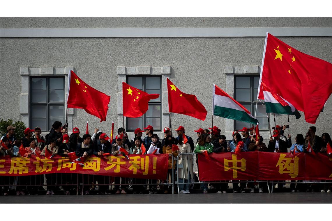 In Budapest schwenken Menschen chinesische und ungarische Fahne. Chinas Präsident Xi Jinping ist zu einem zweitägigen Besuch nach Ungarn gereist. Dort will er mit Ungarns Ministerpräsidenten Viktor Orban mehr als ein Dutzend bilaterale Vereinbarungen beschließen.