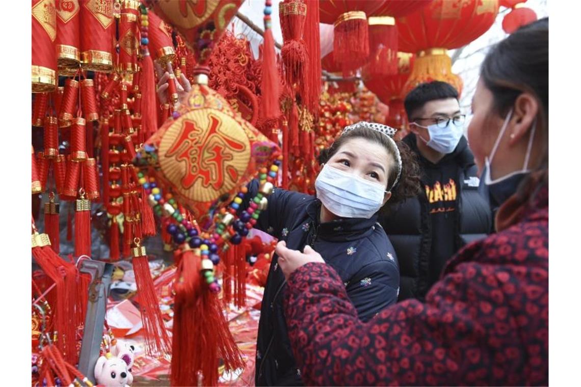 In der zentralchinesischen Provinz Anhui decken sich Menschen auf einem Markt mit Dekoration für das Neujahrsfest ein - und tragen Mundschutz. Foto: CHINATOPIX/AP/dpa