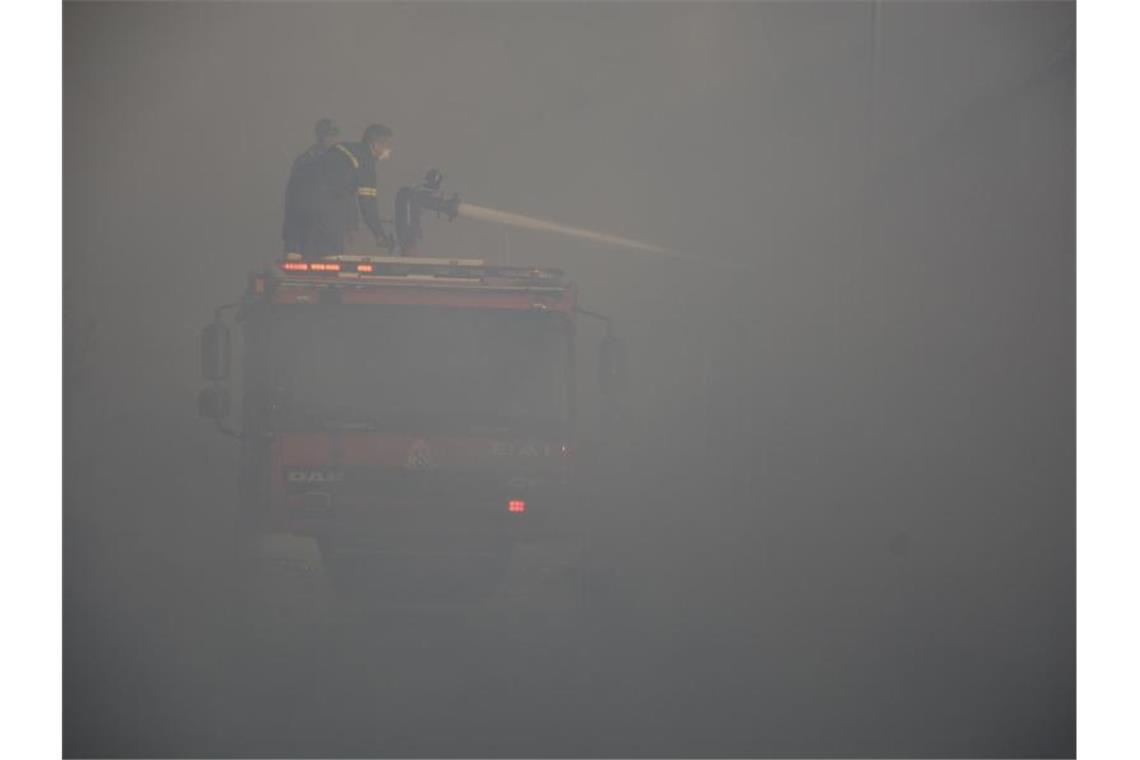 In dichten Rauch gehüllt versuchen Feuerwehrleute, die letzten Glutnester zu löschen. Foto: Panagiotis Balaskas/AP/dpa