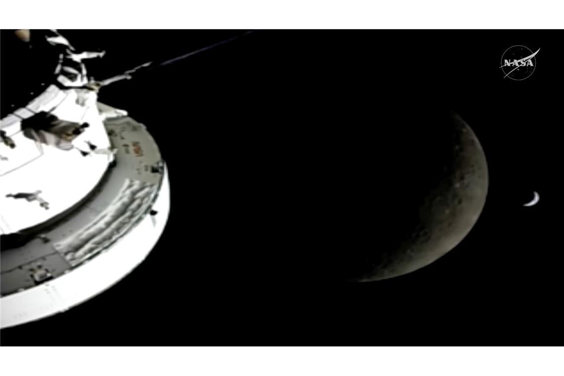 In diesem Bild aus einem von der NASA zur Verfügung gestellten Video sind die "Orion"-Raumkapsel, der Mond und die Erde (r) von einer Kamera aus zu sehen, während die "Artemis 2"-Besatzung und das Raumschiff weiter in den Weltraum vordringen.