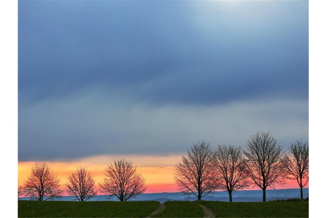 In einem schmalen Streifen färbt die aufgehende Sonne am Morgen den sonst bewölkten Himmel. Foto: Thomas Warnack/dpa