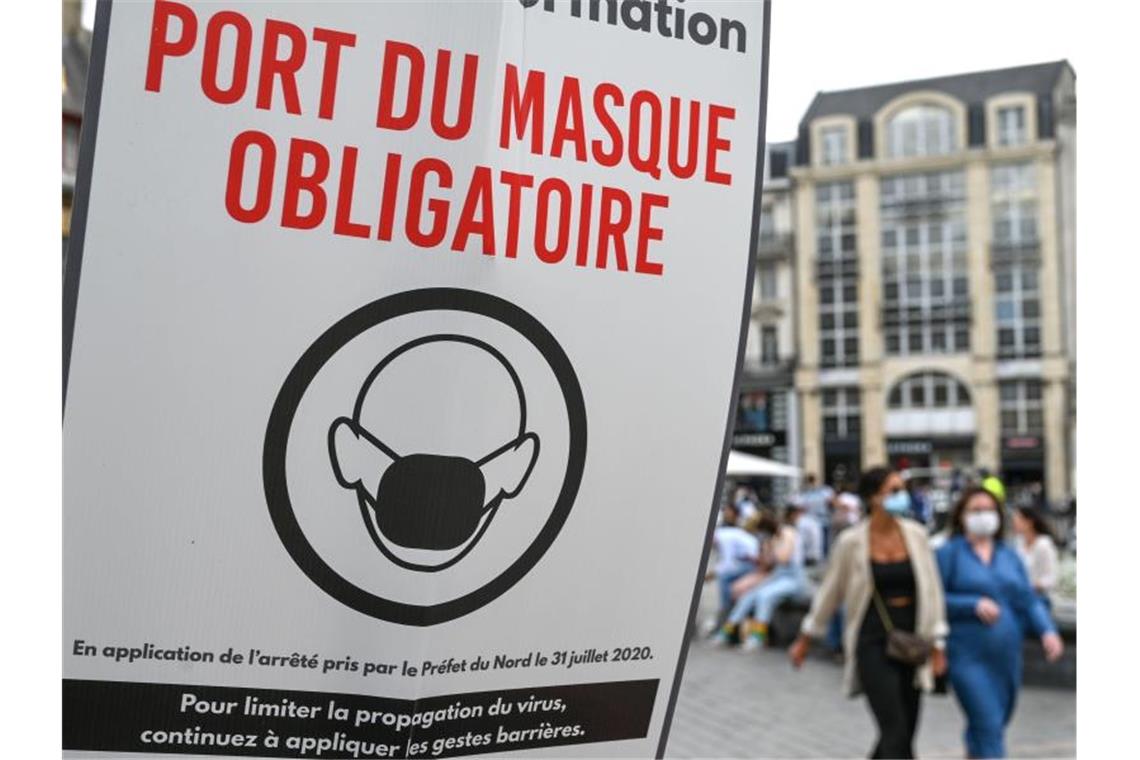 Möglicher Trend in Frankreich: Lieber Covid als Spritze? In einer Fußgängerzone von Lille weist ein Schild auf die Maskenpflicht hin. Foto: Denis Charlet/AFP/dpa/Archiv
