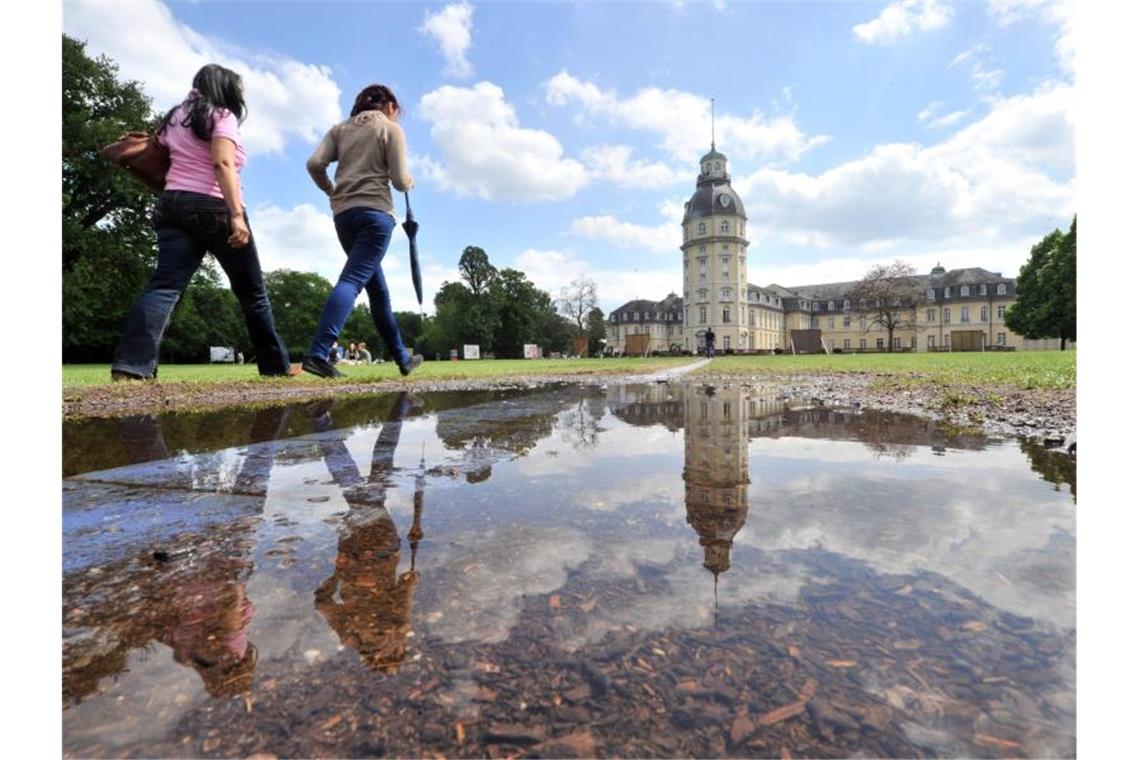 In einer Pfütze spiegelt sich der Karlsruher Schlossgarten. Foto: picture alliance/dpa/Archivbild