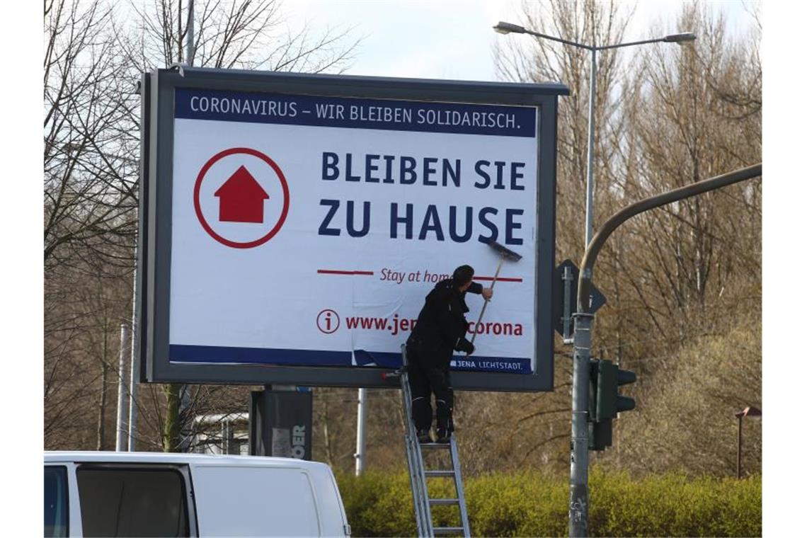 RKI: Coronavirus-Sterberate in Deutschland wird steigen In Jena wird eine Werbefläche mit einem Plakat mit der Aufschrift „Bleiben Sie zu Hause“ beklebt. Foto: Bodo Schackow/dpa-Zentralbild/dpa