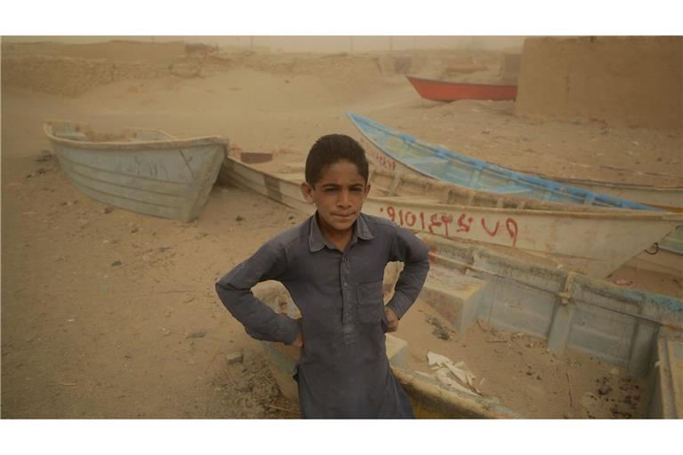 in Junge steht vor alten und zurückgelassenen Booten, wo einst ein See war. Die iranische Provinz Sistan und Belutschistan ist von Trockenheit und Wasserknappheit betroffen.