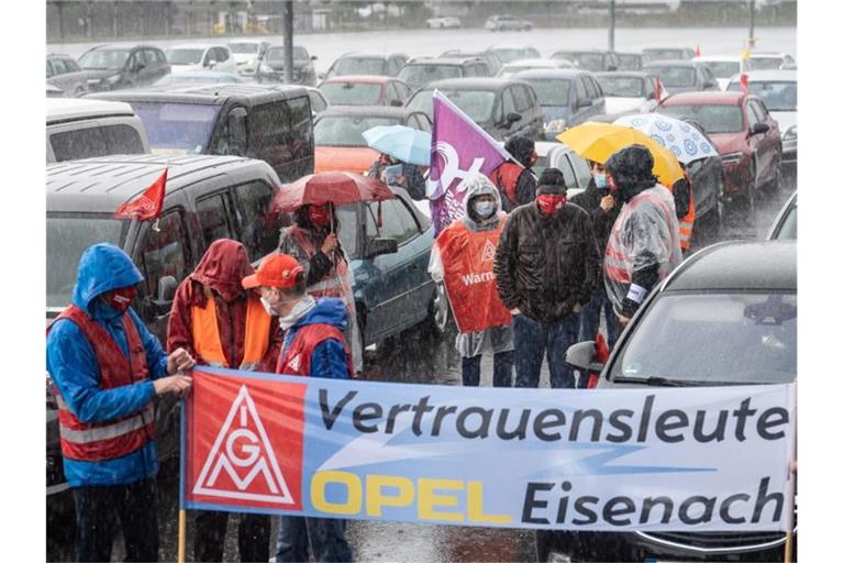 In strömendem Regen stehen Mitarbeiter am Stammsitz des Autobauers Opel oder sitzen in ihren Fahrzeugen, um gegen zunehmenden Druck an ihren Arbeitsplätzen zu demonstrieren. Foto: Frank Rumpenhorst/dpa