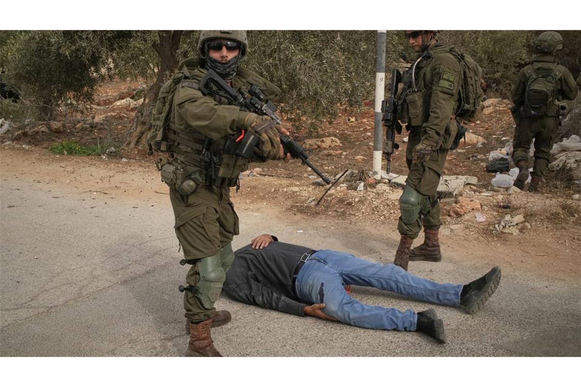 Israelische Soldaten stehen neben einem verwundeten Palästinenser, der auf einer Straße liegt, nachdem sie ihn angeschossen hatten. Dies geschah nach einem Angriff von Siedlern auf Palästinenser, die im Dorf Abu Falah im Westjordanland Oliven pflückten.