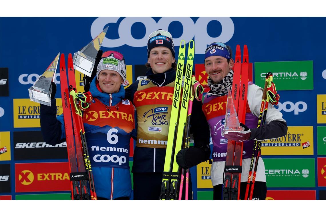 Moch Dritter auf der Alpe Cermis - Carl Gesamt-Achte Johannes Hoesflot Klaebo (M) aus Norwegen jubelt neben dem Zweitplatzierten Mika Vermeulen (l) aus Österreich und dem Drittplatzierten Hugo Lapalus aus Frankreich auf dem Podium der Tour de Ski.