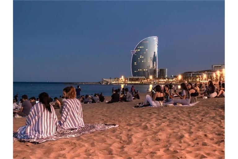 Junge Menschen sitzen in Barcelona, Katalonien, mit Abstand voneinander am Strand. Foto: Paco Freire/SOPA Images via ZUMA Wire/dpa