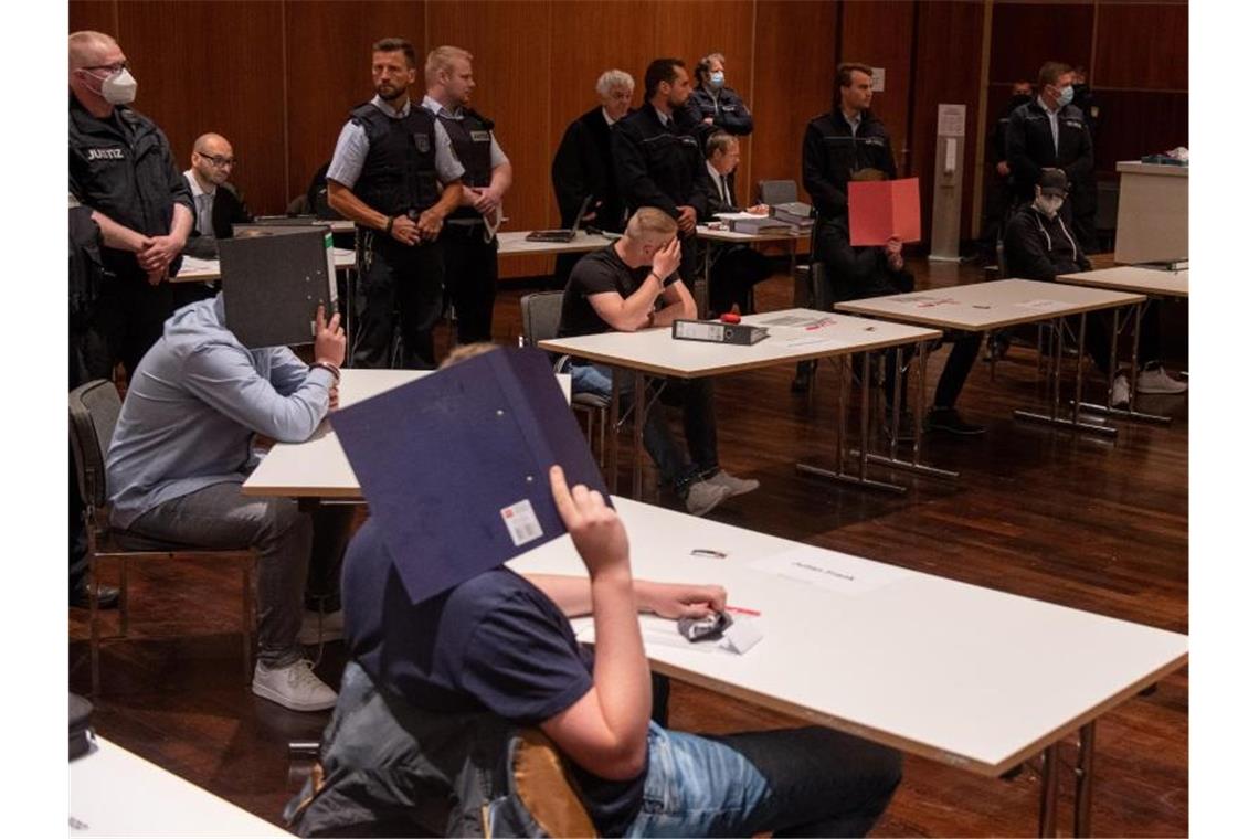 Justizwachtmeister stehen im Kornhaus hinter jungen Männern, die sich Aktenordner vor das Gesicht halten und wegen versuchten Morders angeklagt sind. Foto: Stefan Puchner/dpa