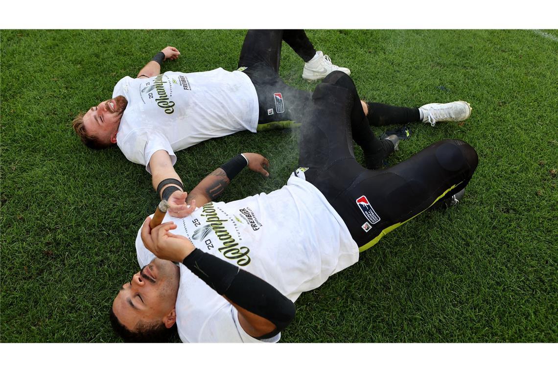 Skibrille, Zigarre und Bier – die besten Bilder der jubelnden Surge-Spieler Kai Hunter (unten) und Luis Bach liegen auf dem Rasen der MHP-Arena.