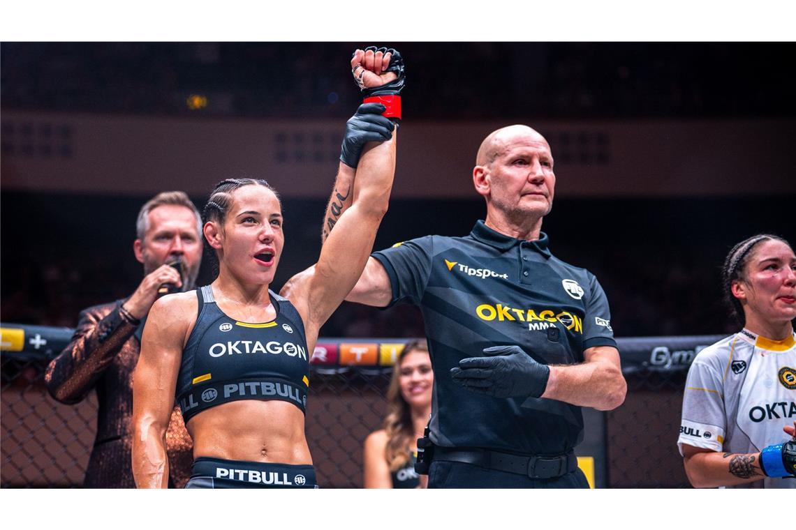 Kampfrichter Gerd Richter hebt den Arm der Siegerin Alina Dalaslan. Clara Ricignuolo (re.) musste sich geschlagen geben, Oktagon-Mitbegründer Ondrej Novotny (li. im Hintergrund) verkündet das Ergebnis.