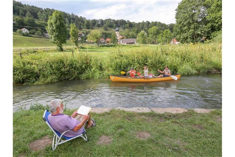 Kanufahrer paddeln auf der Großen Lauter an einem Mann vorbei, der ein Buch liest. Foto: Thomas Warnack