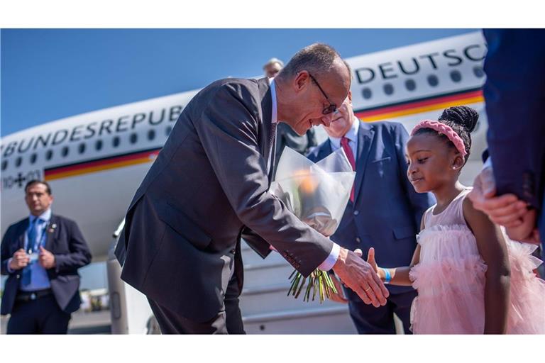 Kanzler Friedrich Merz wird auf dem Flughafen von Johannesburg von einem Mädchen begrüßt.