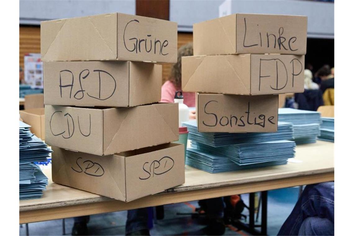 Kartons mit den Aufschriften der verschiedenen Parteien stehen während der Stimmzettelauszählung auf einem Tisch. Foto: Georg Wendt/dpa