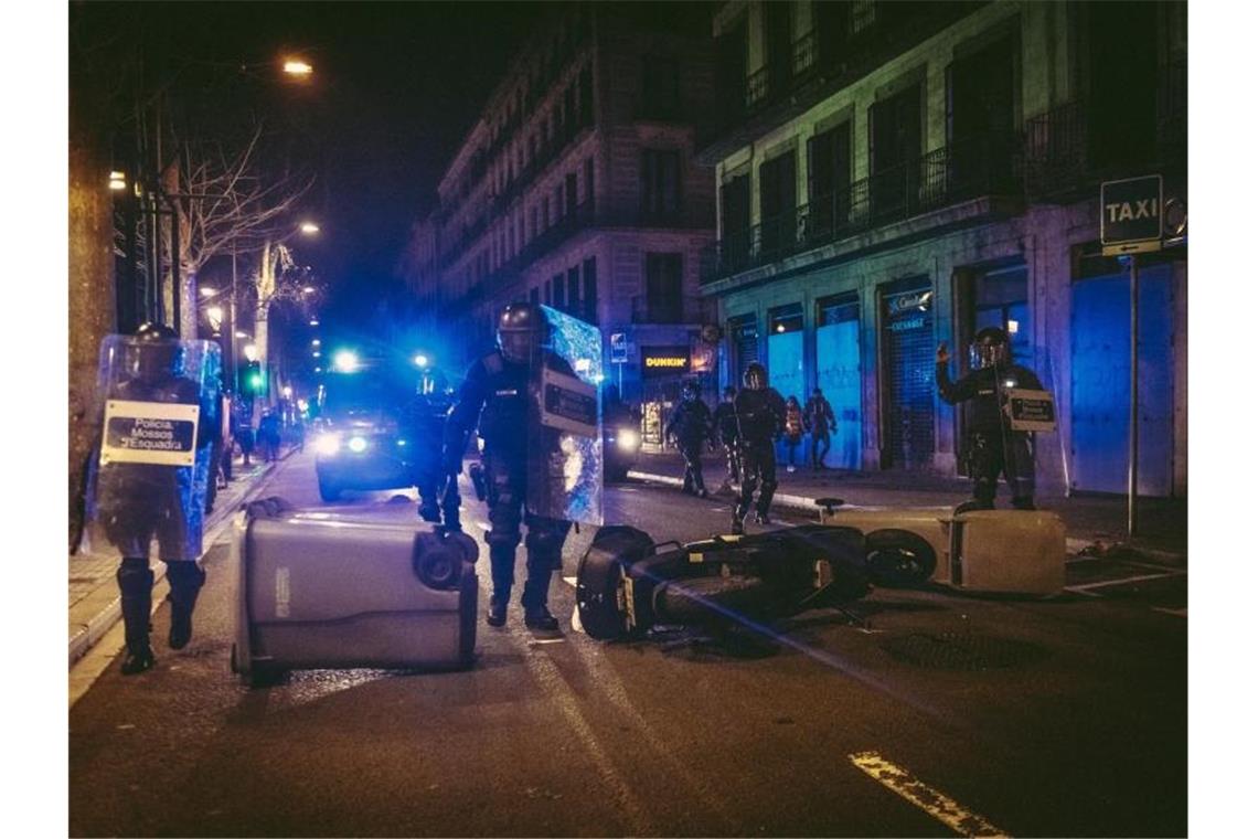 Katalanische Bereitschaftspolizei gehen in Barcelona eine Straße entlang, auf der Protestler Mülltonnen und einen Motorroller umgekippt haben. Foto: Matthias Oesterle/ZUMA Wire/dpa