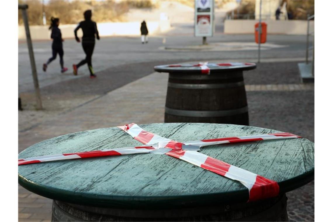 Kein gemütliches Beisammensein: Mit einem rot-weißen-Flatterband sind Stehtische an der Promenade des Ostseebades Warnemünde abgeklebt. Foto: Bernd Wüstneck/dpa-Zentralbild/dpa